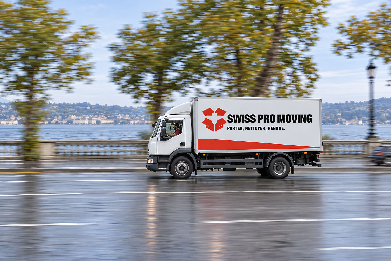 Le camion Swiss Pro Moving roule le long d’un quai de Genève ; les platanes et la rive d’en face sont filés par la vitesse.