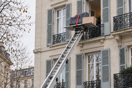 Un monte-meubles déployé contre une façade, la plateforme chargée à hauteur d’un balcon.