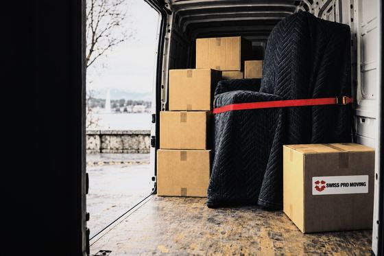 Un fourgon ouvert, chargé de cartons et d’un meuble sous couverture tenu par une sangle rouge.
